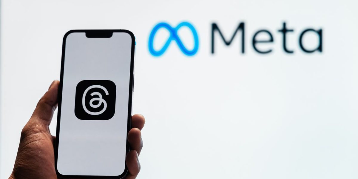 A hand holding a smartphone showing the Threads app with Meta logo in the background.